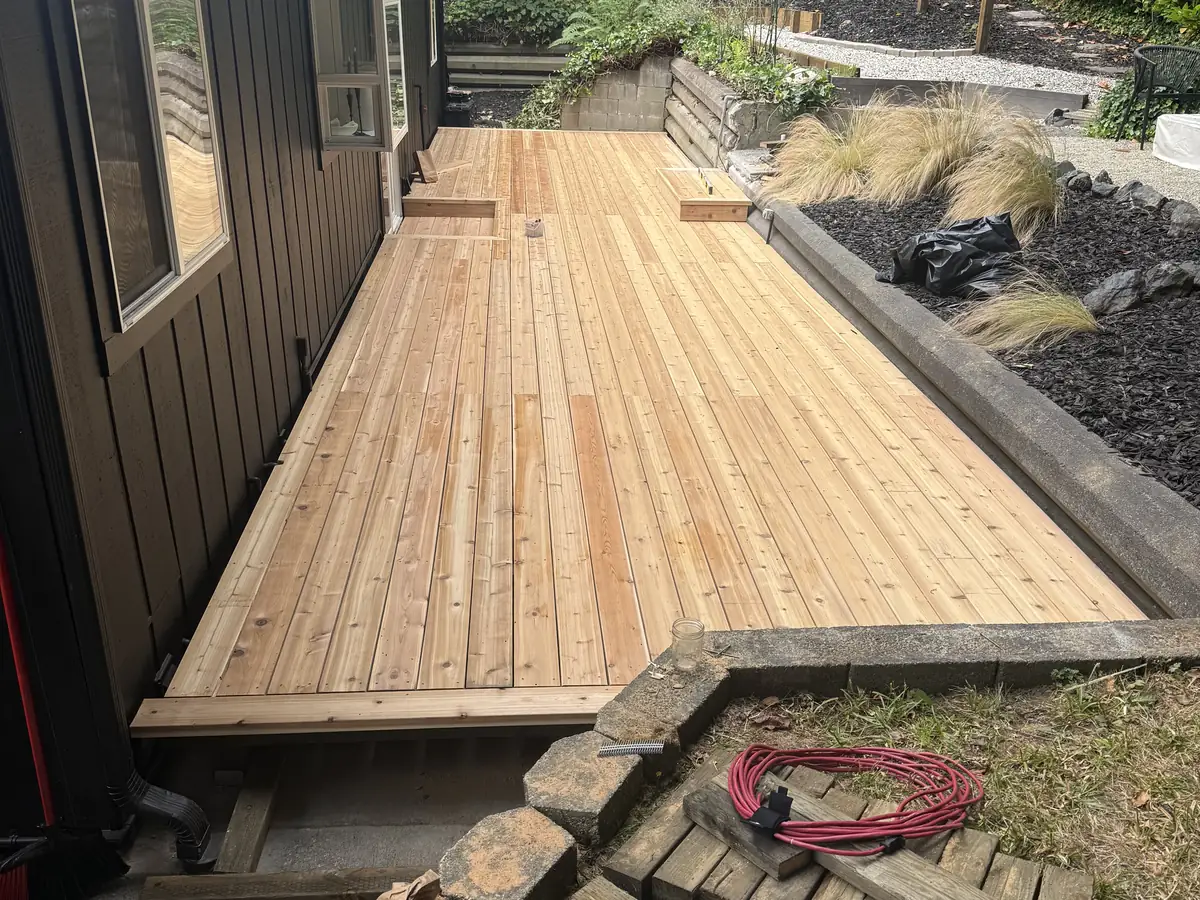 A new wood deck along a dark-sided house, with stone steps below it
